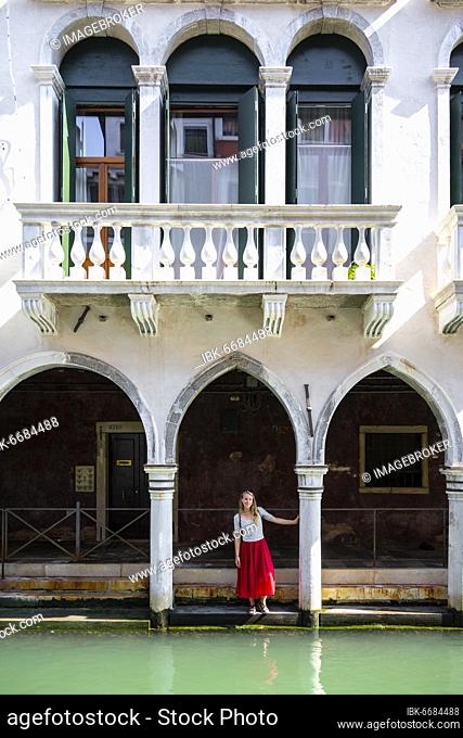 Young woman standing in a portico by a canal, Venice, Veneto, Italy, Europe