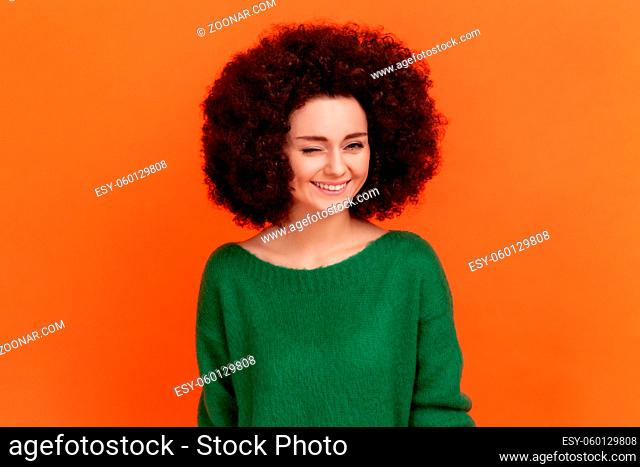 Good looking friendly woman with Afro hairstyle wearing green casual style sweater standing and winking playfully, positive expression
