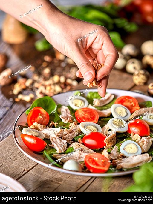 Woman put nuts to a freshly prepared homemade salad from organic ingredients on a wooden board. Natural freshly organic dieting food