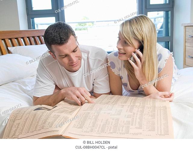 Couple check stocks and shares in bed