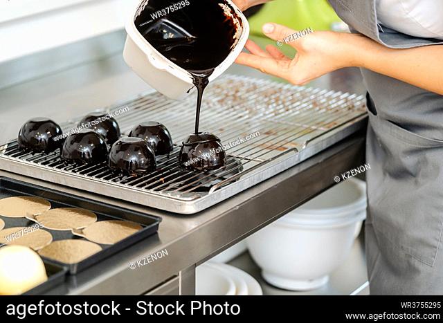 Pastry chef pouring liquid dark chocolate over a sweet dessert