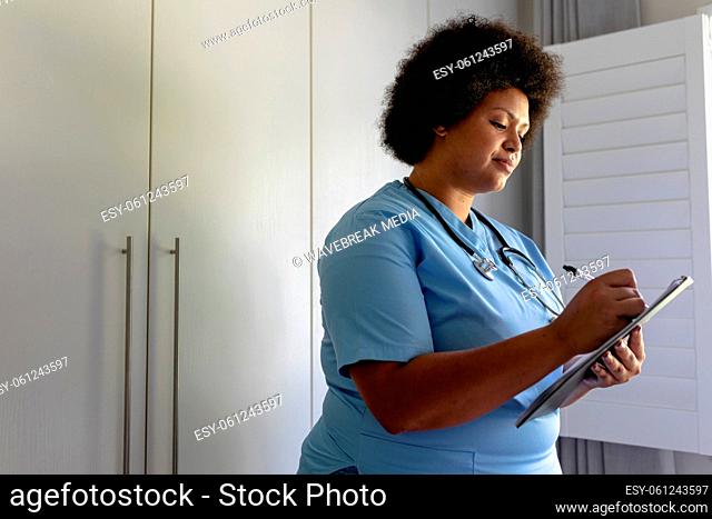 Smiling african american mid adult female nurse writing on clipboard in hospital