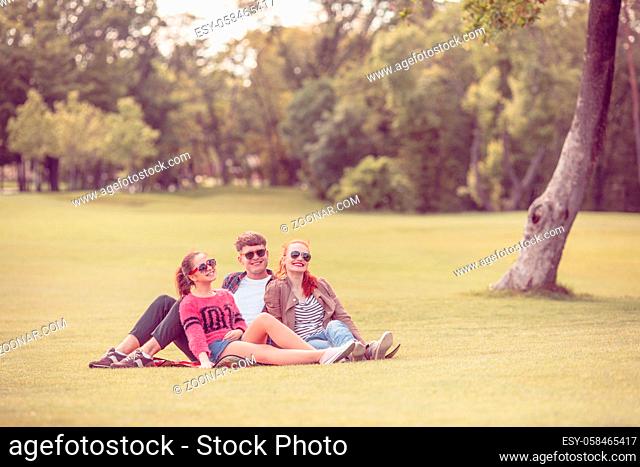 Friendship, leisure, summer and people concept. Group of smiling friends outdoors sitting on grass in park