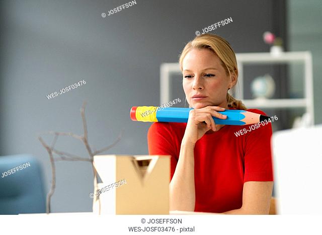 Young woman in office with oversized pen and architectural model on desk
