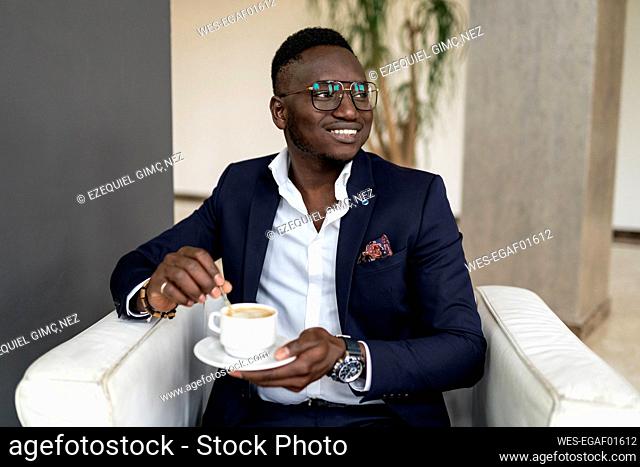 Smiling male professional looking away while holding coffee cup in hotel lobby