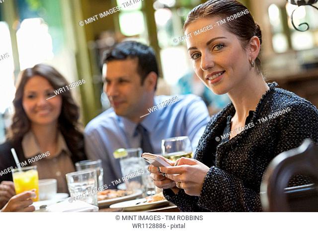 Business people outdoors, keeping in touch while on the go. Three people around a cafe table, one woman turning around, holding a wine glass