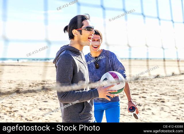 Happy male friends playing beach volleyball on sunny beach