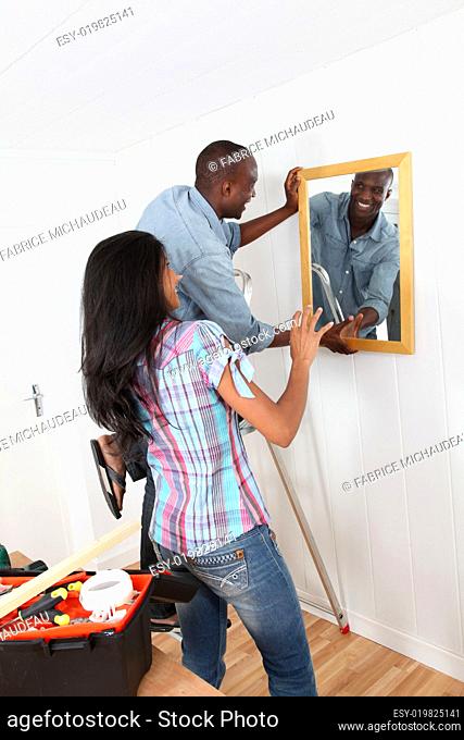 Young couple hanging mirror on the wall