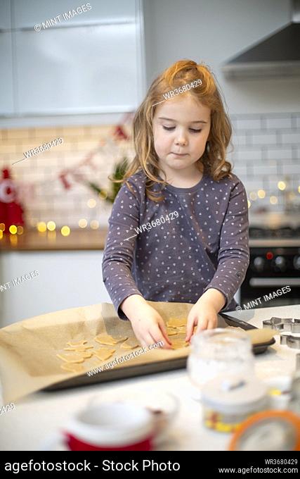 Girl standing in kitchen, baking Christmas cookies