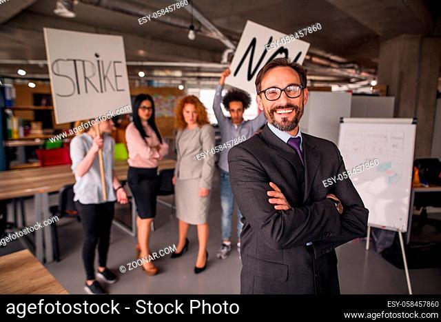 Modern office concept, director standing with his back to striking cowokers. unhappy employees holding posters with words strike and no