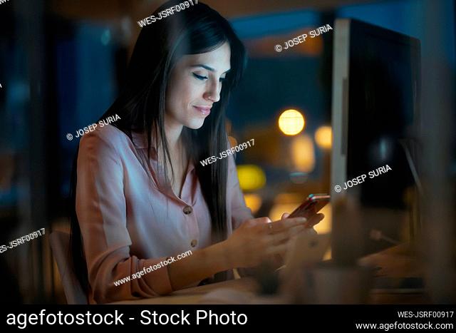 Young woman sitting at desk in office looking at smartphone