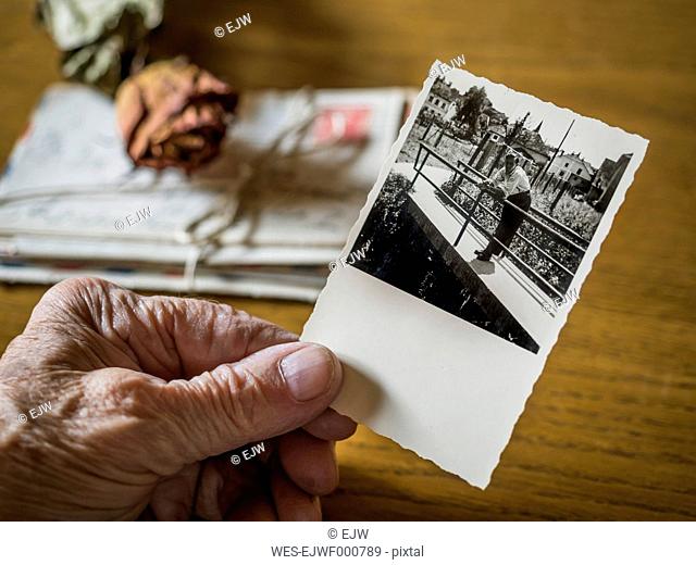 Old woman holding picture of her boyhood friend in hand, old letters and dried rose