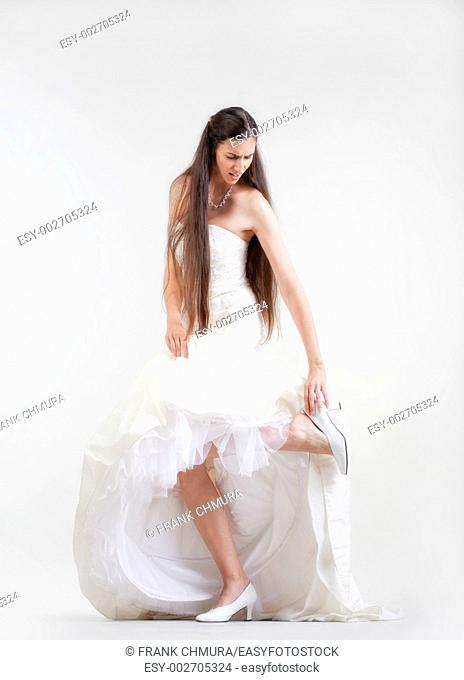 bride in wedding dress taking off her shoe checking her hurting foot