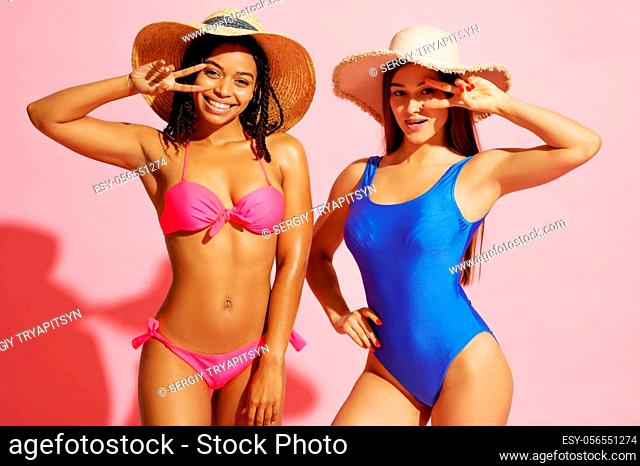 Glamour women in swimsuits and hats poses on pink background in studio. Girls in swimwear ready to take a tan. Models with slim body in swimming underwear