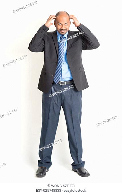 Full body mature Indian business man hands scratching his bald head , standing on plain background