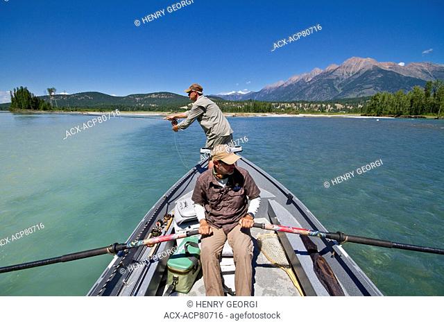 Middle-aged man fly-fishing on Kootenay river with guide rowing fishing boat, East Kootenays, BC, Canada