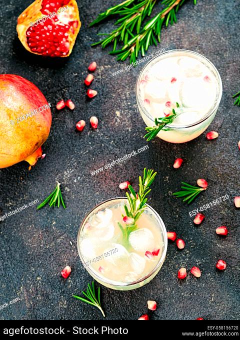 Autumn and winter cocktails idea - white sangria with rosemary, pomegrante and lemon juice and ingredients on black cement background. Copy space