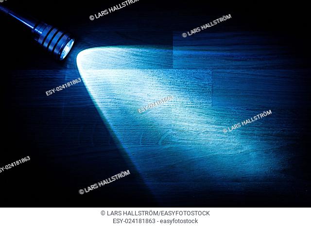 Flashlight and a beam of light in darkness. A modern led light with bright projection on dark wood table. Surface with copy space