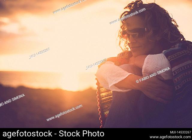 Side portrait of young pretty woman enjoying sunset time alone hugging her knees and loving herself. Female people smile and relax during the evening sunny dusk
