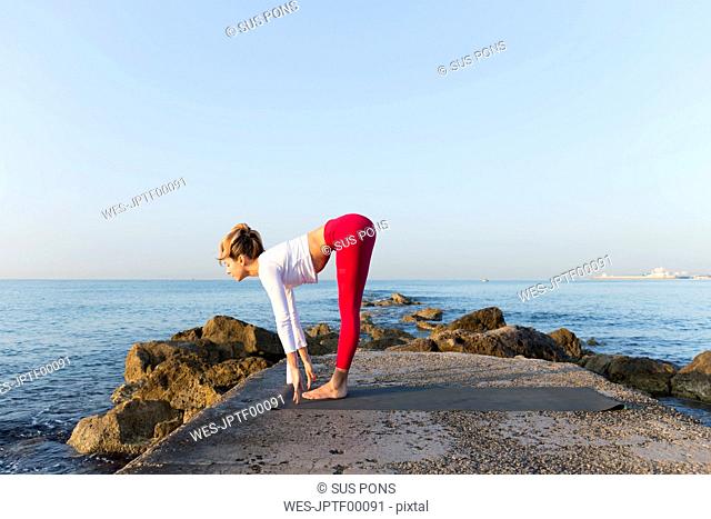 Young woman practicing yoga on the beach, doing sun salutations
