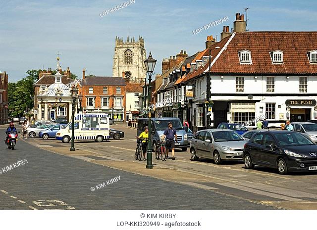 England, East Riding of Yorkshire, Beverley, Two cyclists walk their bicycles past Market Cross in Saturday Market, Beverley