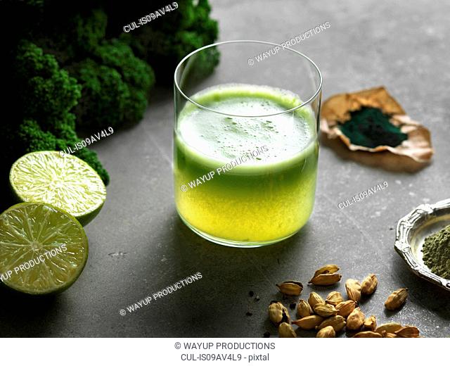 High angle view of green raw juice with halved lime and nutritional supplement