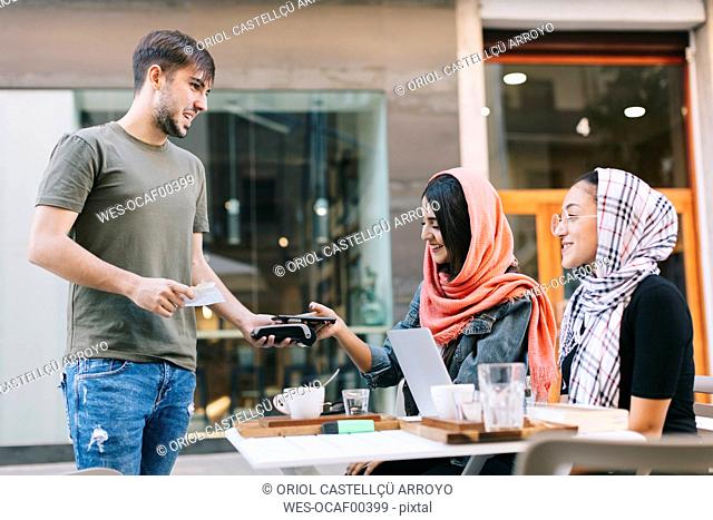 Young woman paying cashless with smartphone in a cafe
