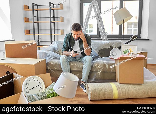 sad man with smartphone and boxes moving home