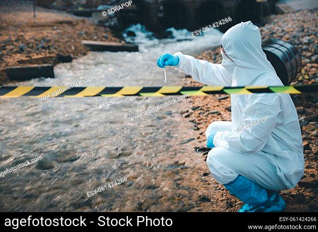 Scientist or Biologist in a protective suit and protect mask collects sample of waste water from industrial for analyze, problem environment