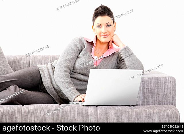 Woman lying on sofa at home working on laptop computer. Isolated on white background