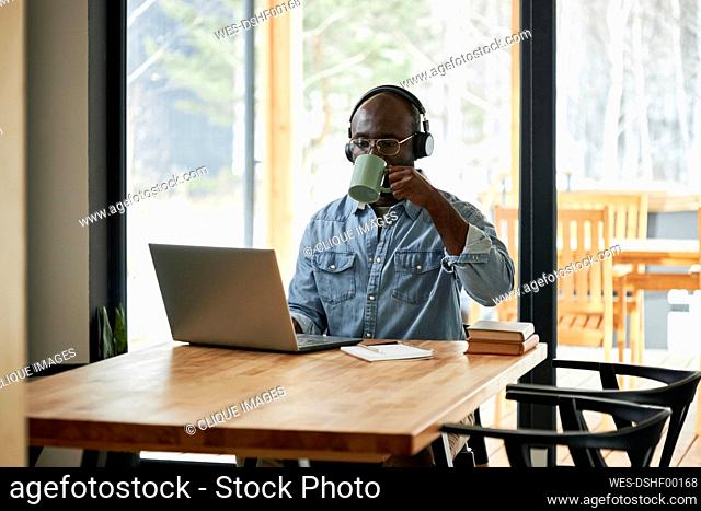 Young businessman drinking tea using laptop sitting at dining table at home