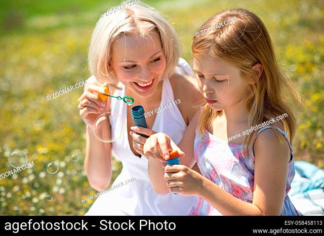 Mother and child playing with bubble blower outdoors. Mom and her child girl enjoying summer time