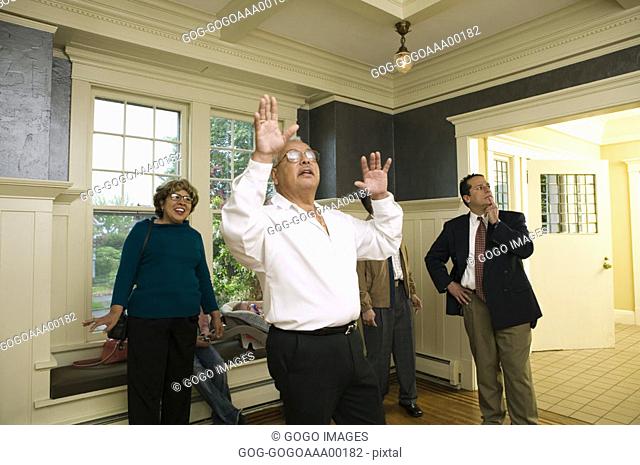 Senior man standing with hand raised, family looking at him