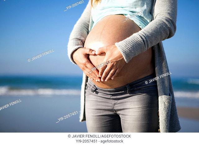 pregnant woman drawing a heart with her hands on her belly