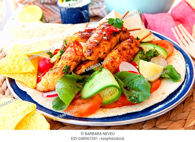 Spicy grilled chicken skewers with fresh salad on tortillas