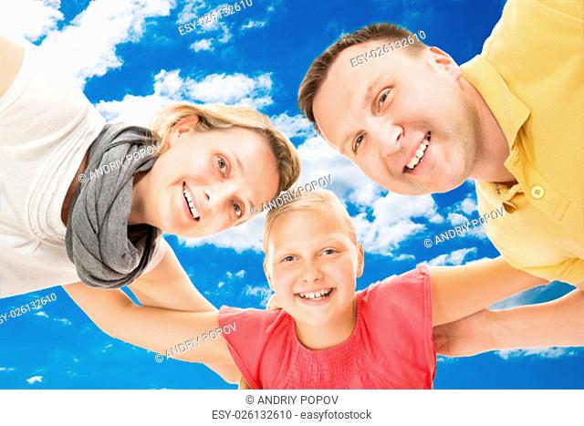 Low angle portrait of happy parents with daughter forming huddle against sky