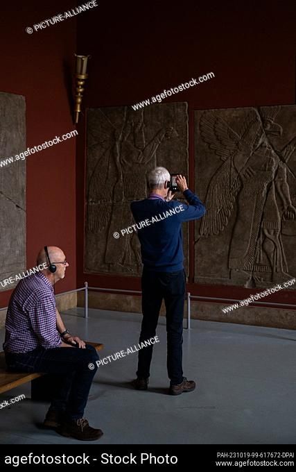 PRODUCTION - 17 October 2023, Berlin: Visitor Jörg sits in the Pergamon Museum in the Assyrian palace room behind visitor Matthias who photographs exhibits