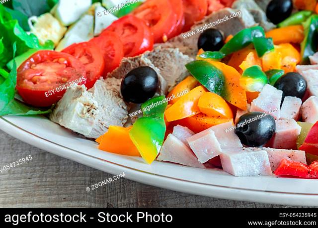 A popular dish of American cuisine - Cobb salad, consisting of greens, eggs, tomatoes, cheese, meat products, stacked in rows on a wide dish and poured sauce