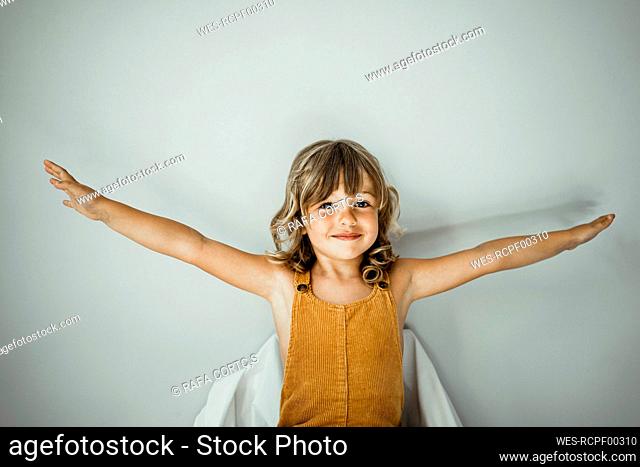 Little girl with arms outstretched standing against wall at home
