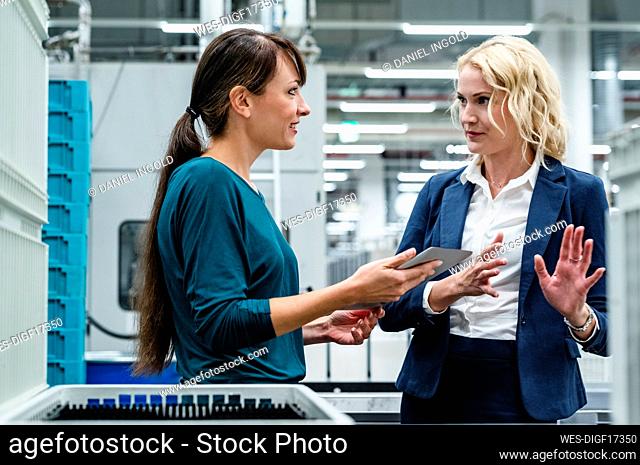 Businesswoman discussing with colleague holding tablet PC In industry
