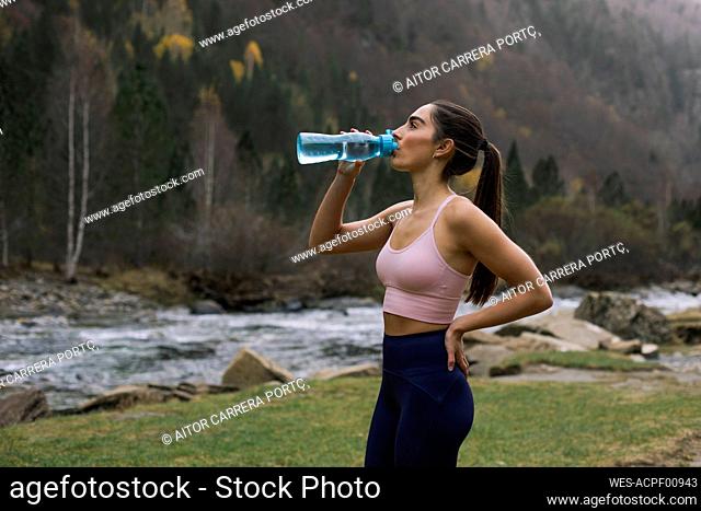 Exhausted young woman drinking water while standing with hand on hip, Ordesa National Park, Huesca, Spain