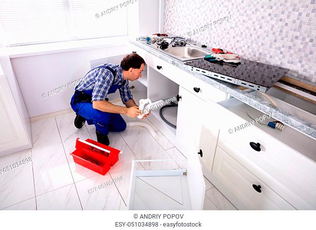 An Overhead View Of Male Plumber Installing Sink Siphon In Domestic Kitchen