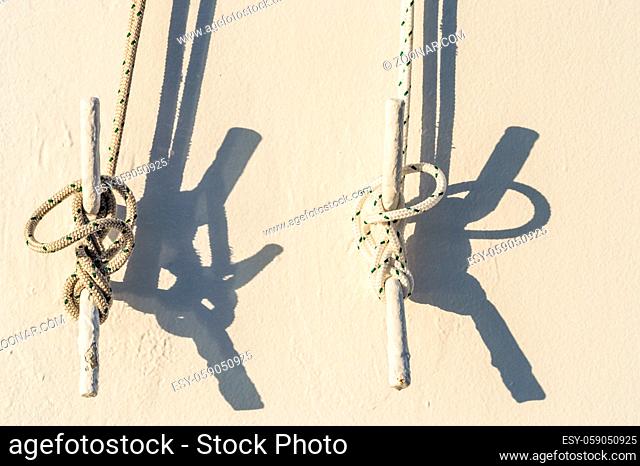 Two nautical ropes tied with marine knots to metal cleats on white exterior wall of cruise ship in morning sunlight