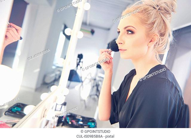 Young female model applying blusher for photo shoot