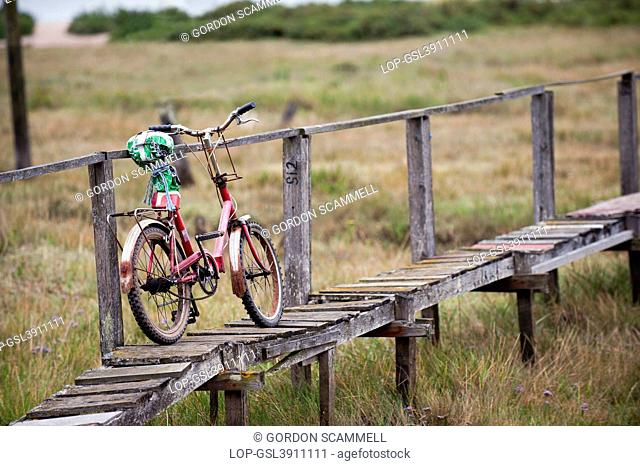 England, Essex, Mersea Island. An old bicycle leaning against a rickety wooden handrail on a walkway on Mersea Island, the most easterly inhabited island in the...
