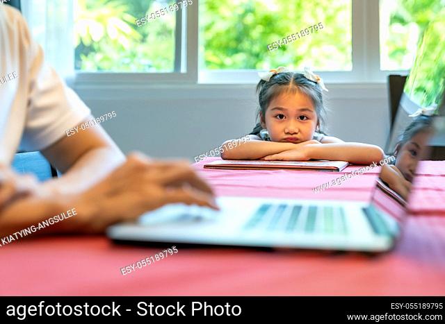 Asian upset girl looking and waiting her father working in dining room. Dad has to working from home while city lockdown from coronavirus covid-19 pandemic