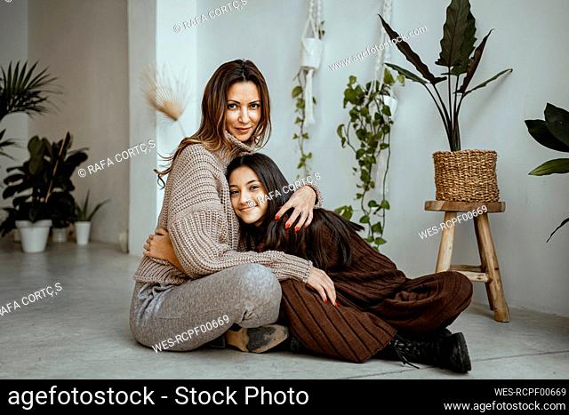 Smiling daughter embracing mother while sitting by potted plant at home