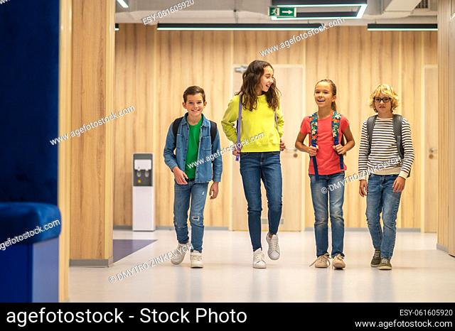 Pupils. Happy boys and girls with school bags looking at camera walking talking in corridor of illuminated room