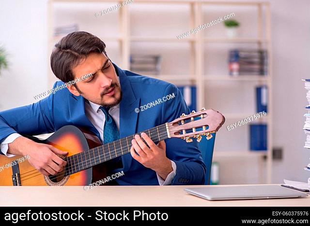 Young businessman employee playing guitar at workplace