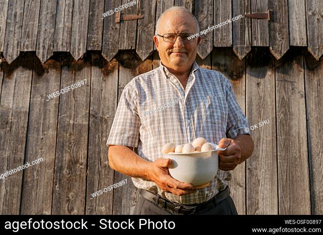 Senior farmer holding bowl of eggs on sunny day